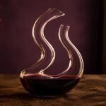 Riedel Mamba snake-shaped crystal wine decanter with a double S-curve, partially filled with red wine, on a dark timber table