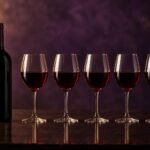 A wine bottle beside five filled glasses in a row