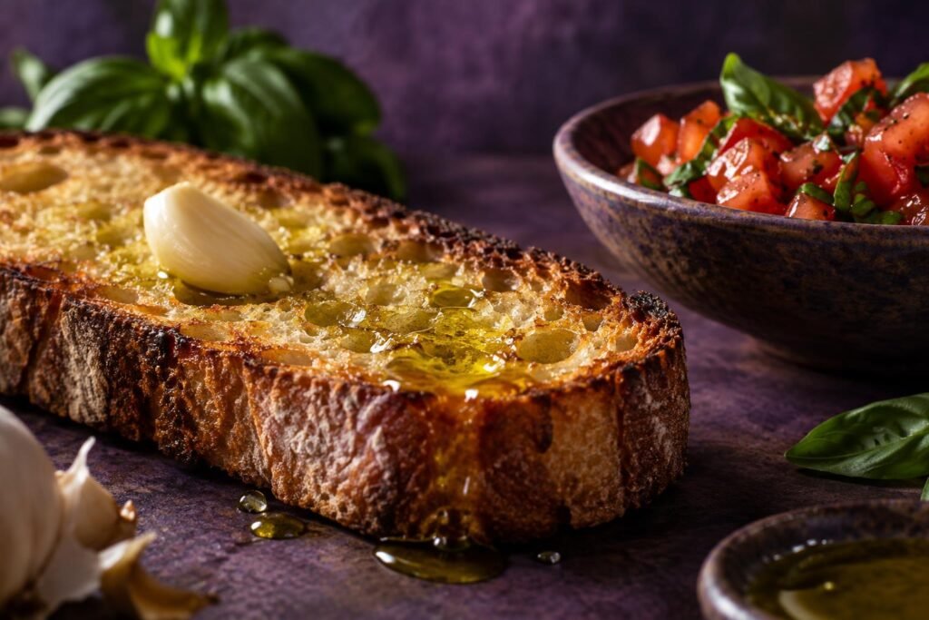 A garlic clove rubbed over hot toasted bread with olive oil and chopped tomato nearby