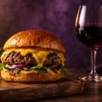 Beef burger with melted cheese beside a glass of red wine